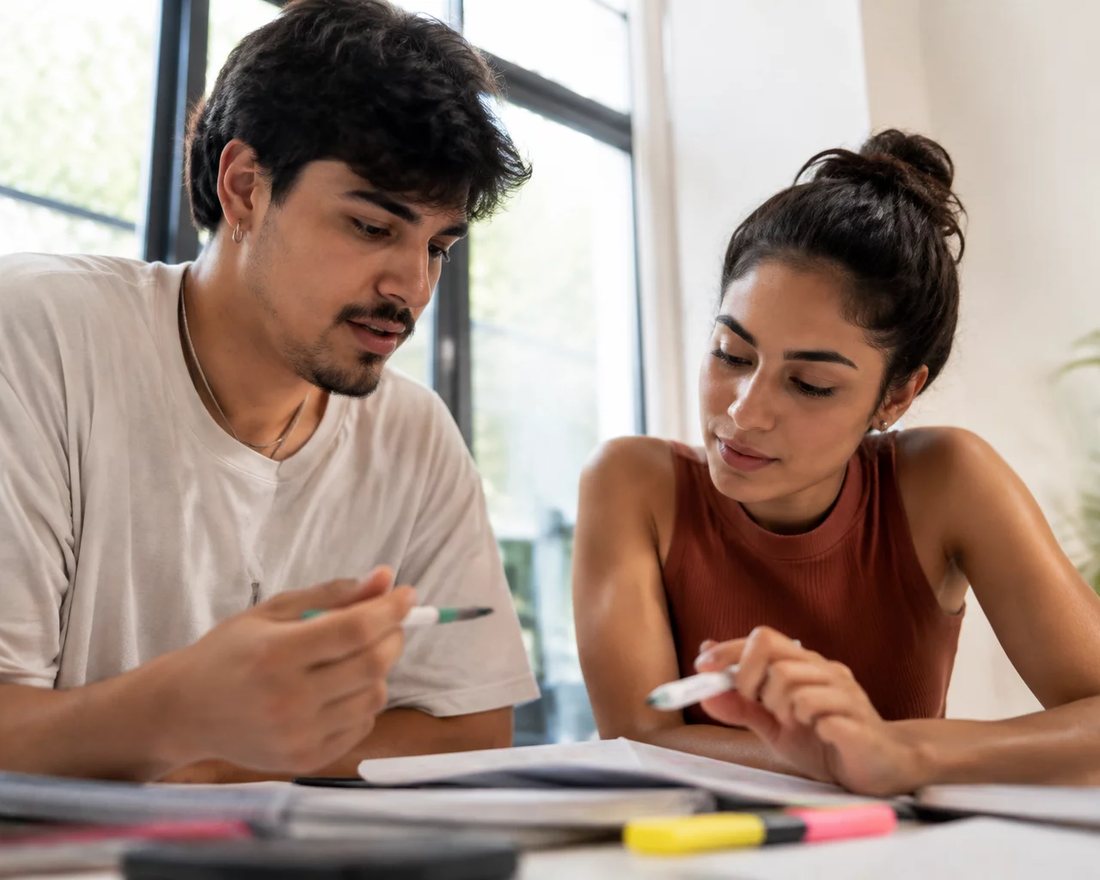 Reunião de trabalho em volta de uma mesa com laptop, papéis e xícaras, alguém defendendo uma proposta